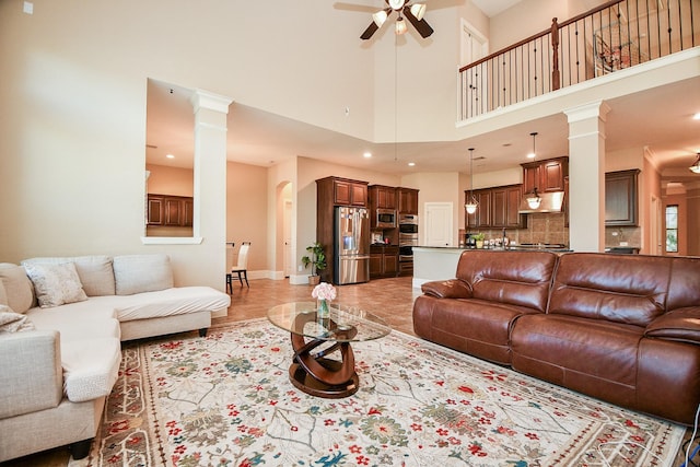 living room featuring baseboards, a high ceiling, a ceiling fan, and decorative columns