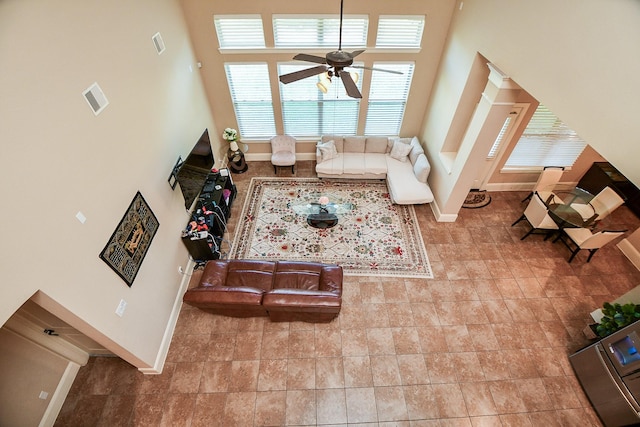 living room featuring visible vents, baseboards, ceiling fan, and a towering ceiling