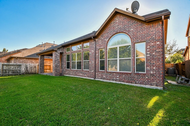 rear view of property featuring central AC, a lawn, brick siding, and a fenced backyard