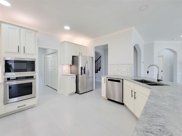 kitchen with appliances with stainless steel finishes, tasteful backsplash, light stone countertops, sink, and white cabinetry