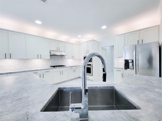 kitchen featuring light stone countertops, sink, backsplash, appliances with stainless steel finishes, and white cabinets