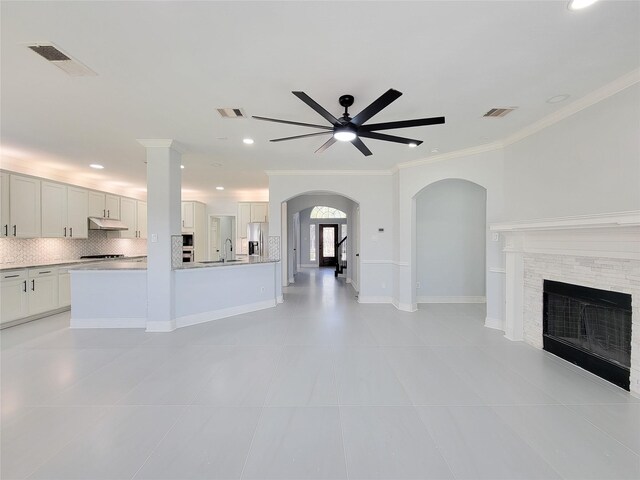 unfurnished living room featuring light tile patterned floors, sink, ceiling fan, crown molding, and a fireplace