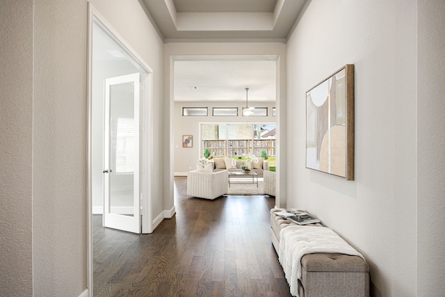 hall with dark wood-style floors, a tray ceiling, and baseboards