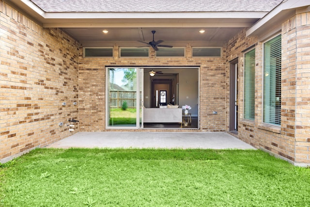 view of exterior entry featuring a yard, roof with shingles, ceiling fan, and brick siding