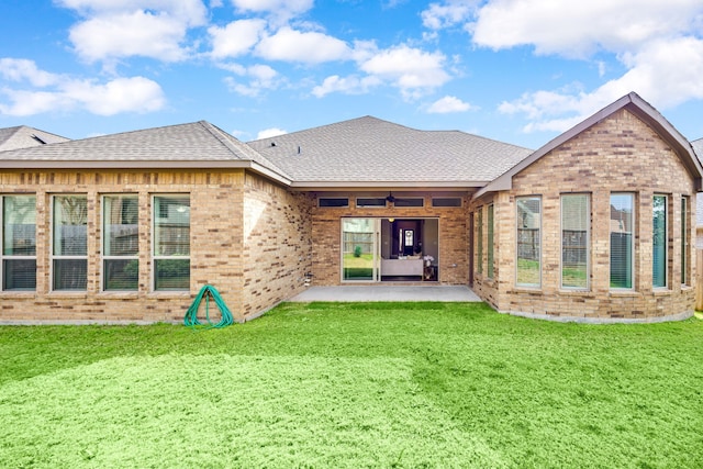 rear view of property featuring ceiling fan, a patio, a shingled roof, and a lawn