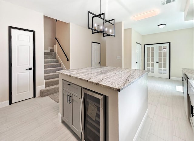 kitchen with a kitchen island, pendant lighting, beverage cooler, light stone counters, and french doors