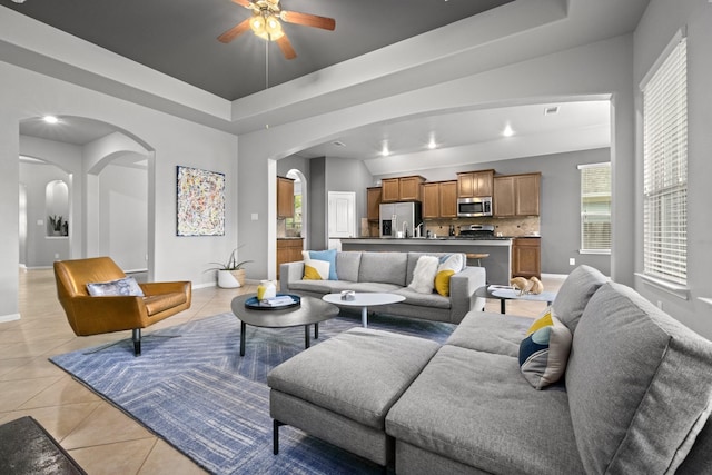 living room featuring arched walkways, baseboards, a tray ceiling, and light tile patterned floors