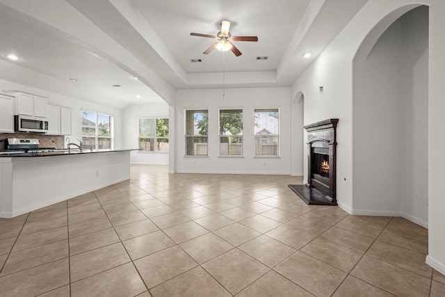114 Kohen Ct, Montgomery, TX 77316 - unfurnished living room with ceiling fan, light tile patterned floors, a lit fireplace, a sink, and a raised ceiling