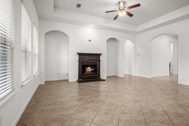 114 Kohen Ct, Montgomery, TX 77316 - unfurnished living room featuring a tray ceiling, a ceiling fan, light tile patterned floors, a warm lit fireplace, and baseboards