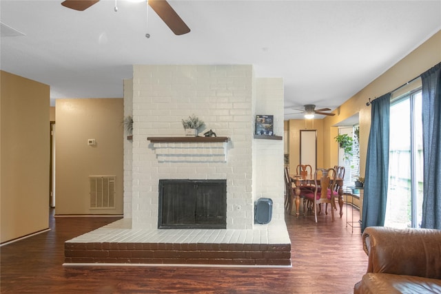 living room featuring a brick fireplace, visible vents, a ceiling fan, and wood finished floors