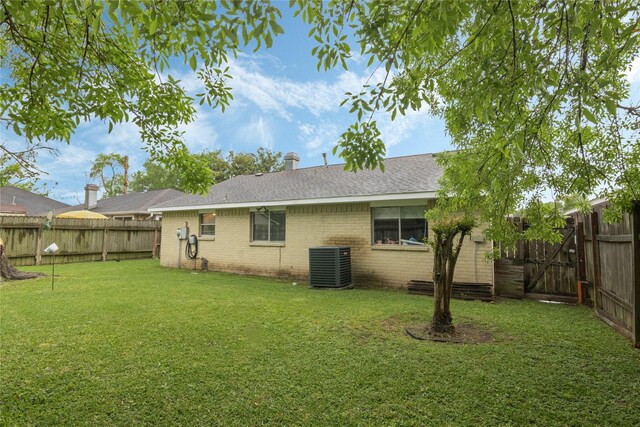 back of property featuring a fenced backyard, brick siding, a lawn, a shingled roof, and cooling unit