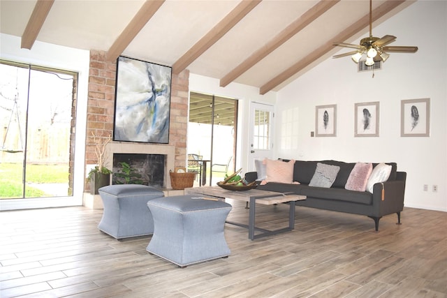 living area with beamed ceiling, plenty of natural light, a fireplace, and light wood finished floors