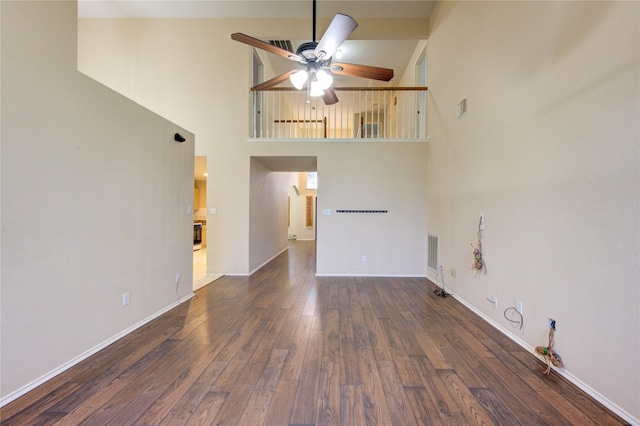 unfurnished living room with dark hardwood / wood-style floors, ceiling fan, and a towering ceiling