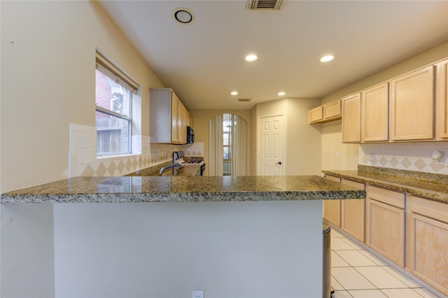 kitchen with light brown cabinetry, light stone counters, light tile patterned floors, range with gas stovetop, and kitchen peninsula