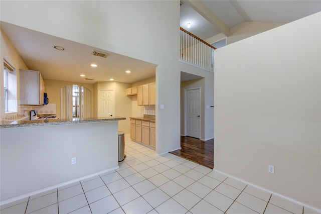 kitchen with light brown cabinetry, tasteful backsplash, light stone counters, high vaulted ceiling, and light tile patterned floors