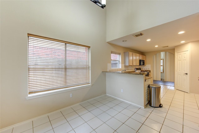 kitchen with light tile patterned flooring, light stone counters, black appliances, kitchen peninsula, and backsplash