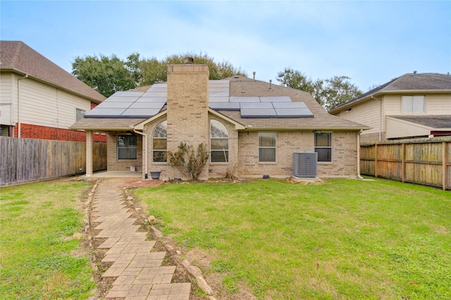 back of property featuring central AC unit, a lawn, and solar panels