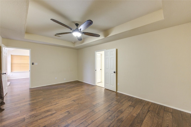 spare room with ceiling fan, a tray ceiling, and dark hardwood / wood-style flooring