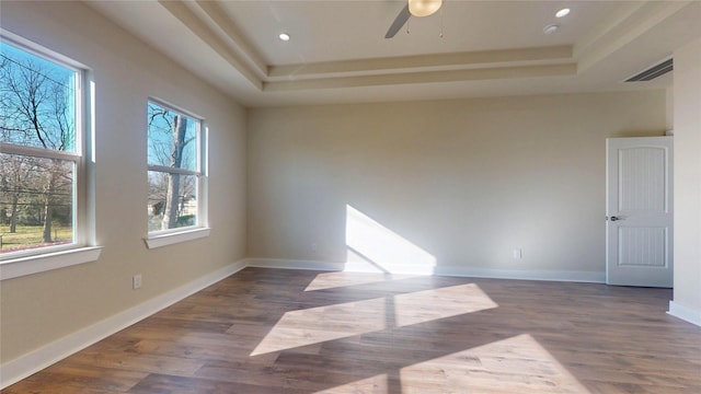 spare room with wood finished floors, a raised ceiling, visible vents, and baseboards