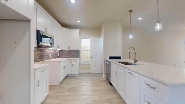 kitchen with stainless steel appliances, a sink, white cabinets, light stone countertops, and pendant lighting