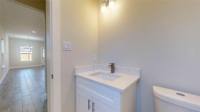 half bath featuring a chandelier, baseboards, vanity, and toilet