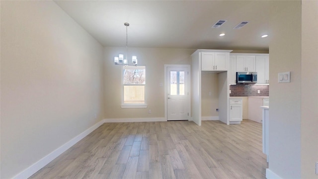 kitchen with visible vents, white cabinetry, light countertops, backsplash, and stainless steel microwave