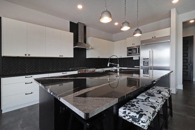 kitchen with a large island, wall chimney range hood, a breakfast bar area, and built in appliances