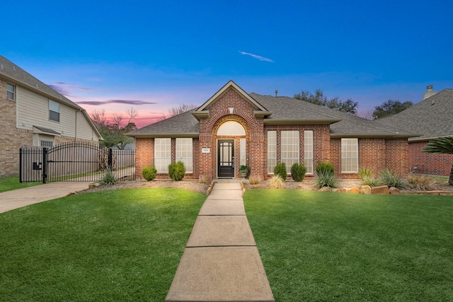 view of front of home with roof with shingles, brick siding, a front lawn, and a gate