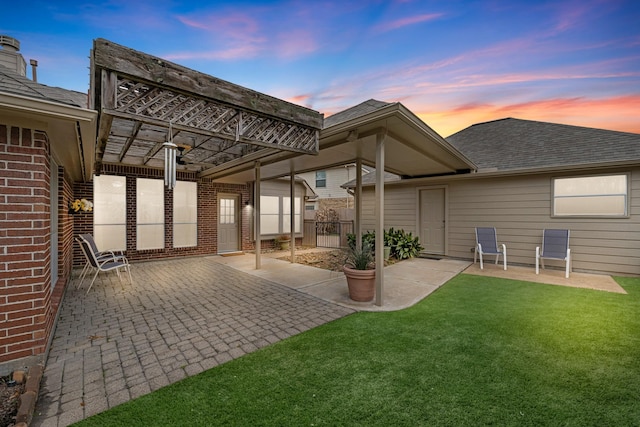 back of house at dusk featuring a patio area, brick siding, a lawn, and fence