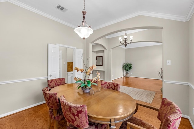 dining space featuring arched walkways, wood finished floors, visible vents, baseboards, and crown molding