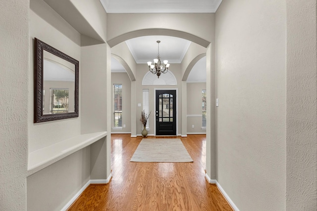 foyer entrance with light wood finished floors, baseboards, ornamental molding, and a chandelier