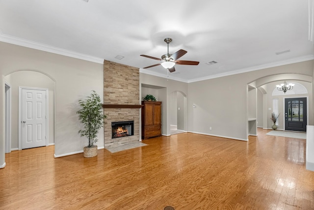 unfurnished living room with arched walkways, a fireplace, visible vents, light wood-type flooring, and ceiling fan with notable chandelier