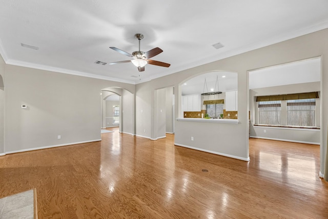 unfurnished living room featuring arched walkways, crown molding, visible vents, light wood-style floors, and a ceiling fan