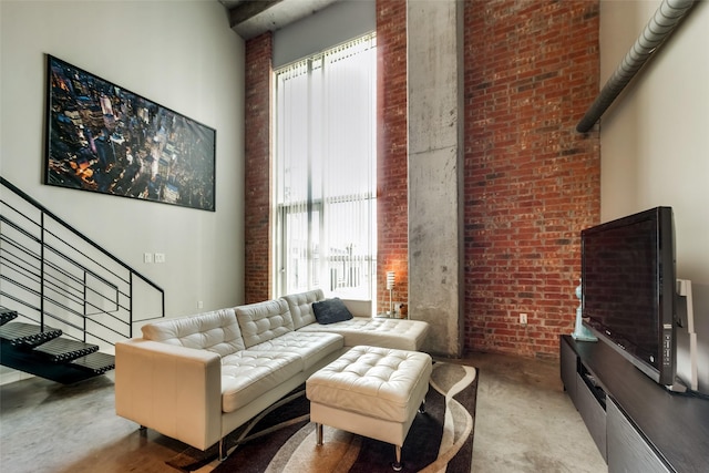 living area with a towering ceiling, brick wall, and stairs