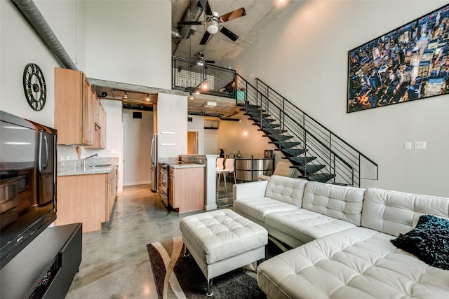 living area with ceiling fan, stairway, concrete floors, and a towering ceiling