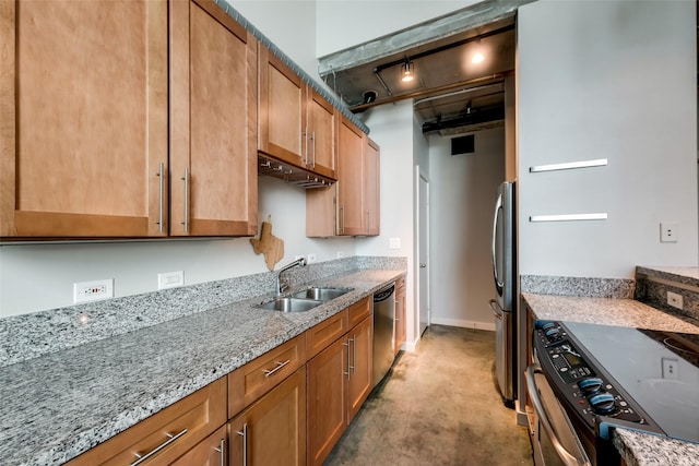 kitchen with brown cabinets, appliances with stainless steel finishes, a sink, light stone countertops, and baseboards