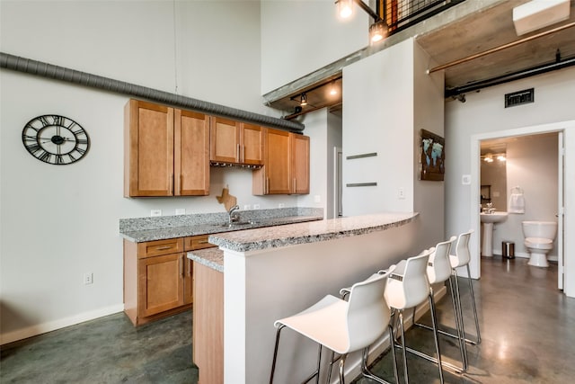 kitchen with visible vents, a towering ceiling, a kitchen breakfast bar, concrete floors, and a sink