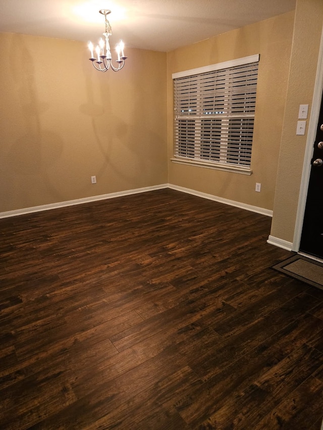 empty room with dark hardwood / wood-style flooring and a chandelier