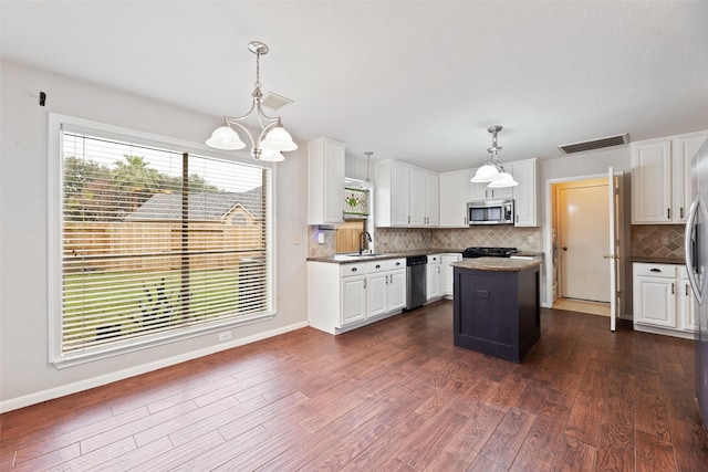 kitchen featuring pendant lighting, stainless steel appliances, visible vents, a kitchen island, and a sink