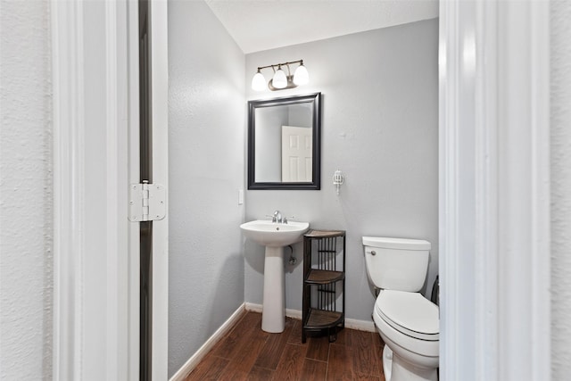 half bathroom featuring a sink, toilet, baseboards, and wood finished floors