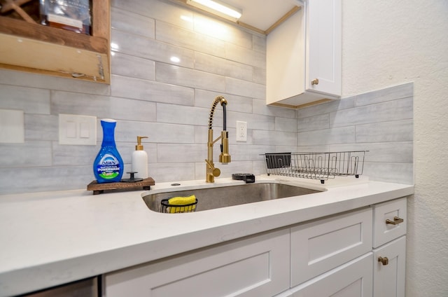 kitchen with tasteful backsplash, light countertops, a sink, and white cabinetry