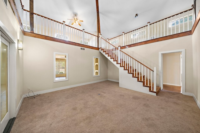 unfurnished living room with a high ceiling, visible vents, baseboards, stairway, and carpet