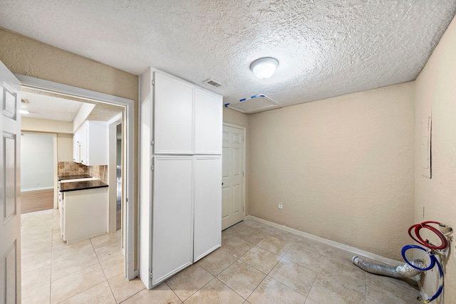 interior space featuring visible vents, a textured ceiling, baseboards, and light tile patterned floors