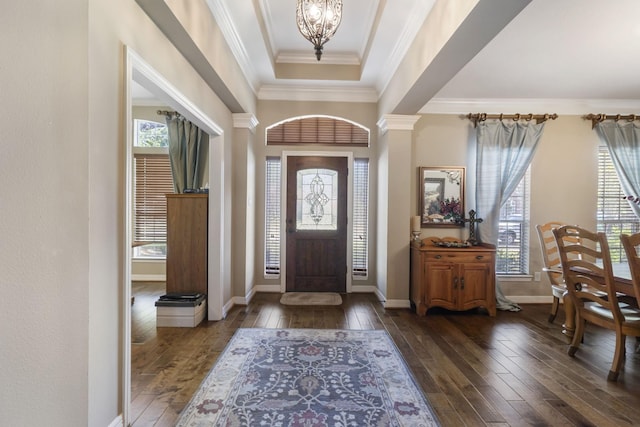 foyer entrance with decorative columns, dark hardwood / wood-style flooring, a notable chandelier, a tray ceiling, and crown molding