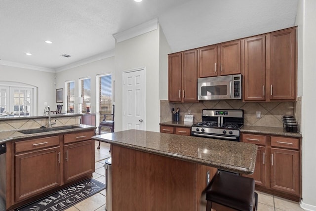 kitchen featuring dark stone countertops, a center island, sink, appliances with stainless steel finishes, and a kitchen bar