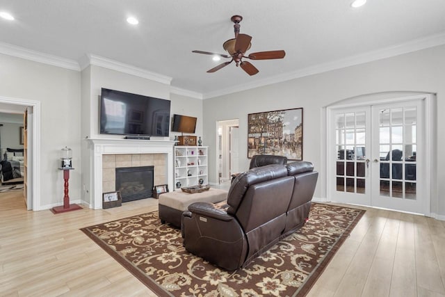 living room featuring light wood-type flooring, french doors, ornamental molding, and a fireplace