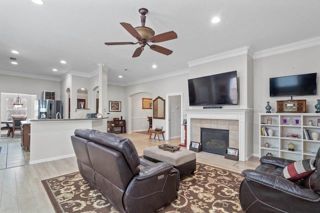 living room featuring a tiled fireplace, crown molding, ceiling fan, and light hardwood / wood-style flooring