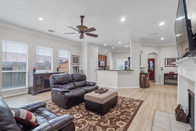 living room featuring light hardwood / wood-style floors, ceiling fan, ornamental molding, and a fireplace