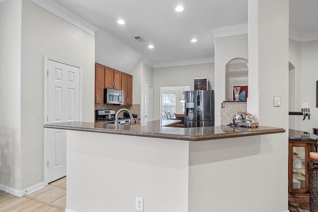 kitchen with dark stone counters, crown molding, stainless steel appliances, kitchen peninsula, and tasteful backsplash