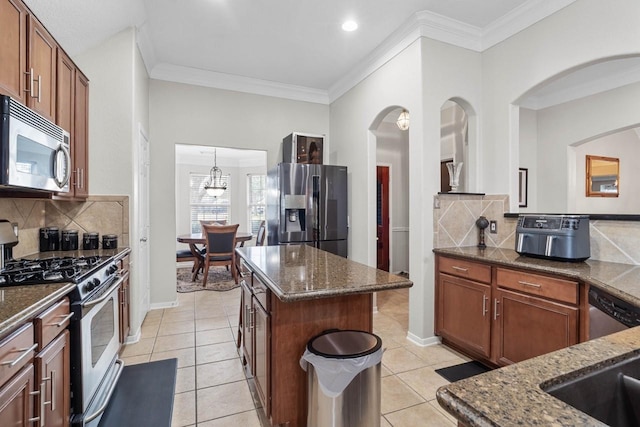 kitchen with appliances with stainless steel finishes, a kitchen island, decorative light fixtures, and dark stone counters